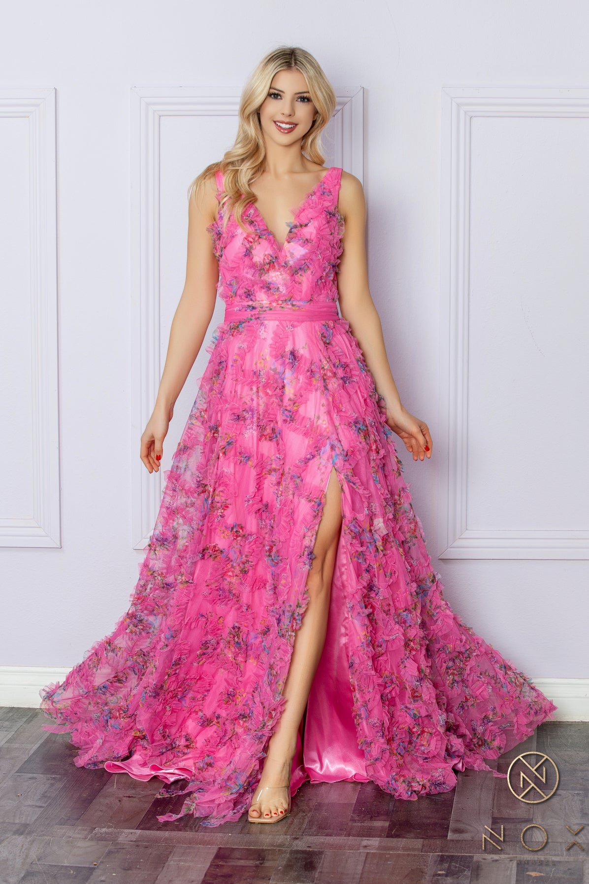 Elevate your formal ensemble with our Nox Anabel E1445 long floral A line dress. Featuring a stunning ruffle detailing and a flattering V neck, this dress is perfect for any prom or formal event. The elegant pleated design and maxi slit add a touch of boho flair to this timeless piece. Sizes: 2-16 Colors: Blue, Fuchsia, Lilac