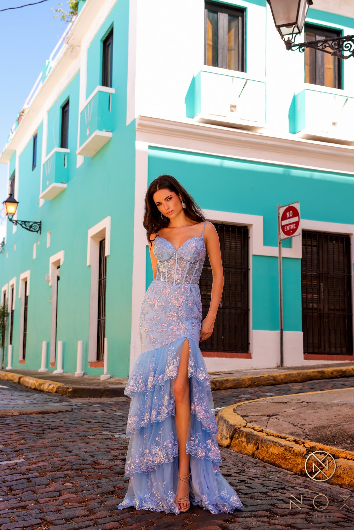 Expertly crafted with a sheer corset and V neck design, the Nox Anabel T1337 dress exudes sophistication. Its sequin maxi slit mermaid skirt, layered asymmetrical lace, and formal silhouette create a unique and eye-catching look. Perfect for any formal occasion, this dress is designed to make you stand out. Sizes: 0-16 Colors: Black, Light Blue, Dark Fuchsia