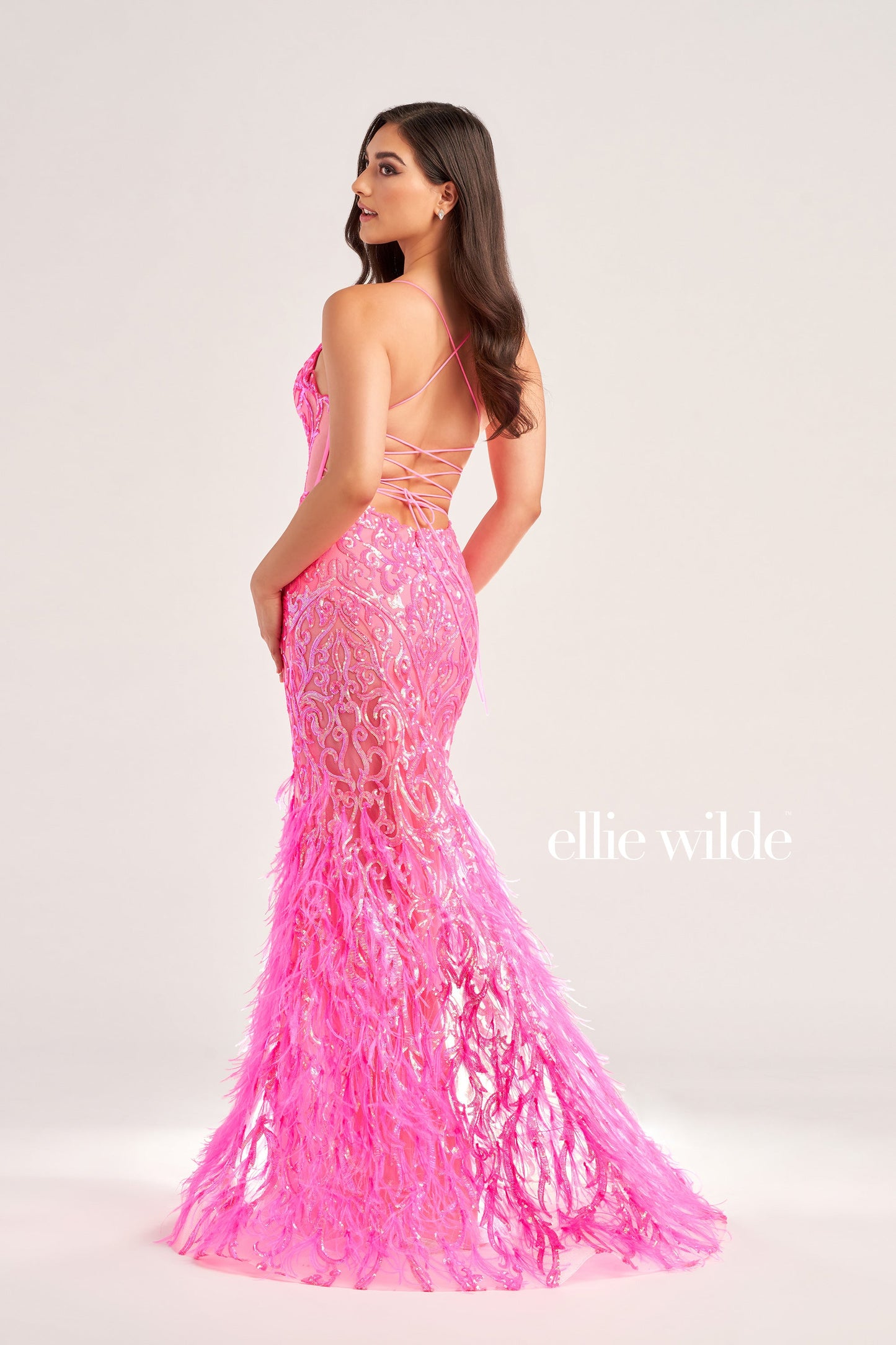 The Ellie Wilde EW35006 Sheer Sequin Prom Dress Gown features a low lace-up back with a side waist mesh inset corset and a glamorous, full-length feather skirt. Look stunning on your special night with this luxurious backless gown. COLOR: ORANGE, CHAMPAGNE, EMERALD, HOT PINK, IRIS SIZE: 00 - 16