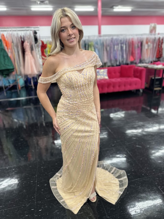 The Nox Anabel H1669 in size 4 is a meticulously crafted champagne-colored gown designed for formal occasions. Its long, fitted silhouette is enhanced by detailed beadwork and sequins, offering a refined shimmer that catches the light elegantly. The gown features a sophisticated slit, providing both movement and subtle allure. A standout element is the detachable asymmetrical off-the-shoulder cape sleeve, which adds versatility and a modern edge to the classic design. This dress combines expert tailoring wi