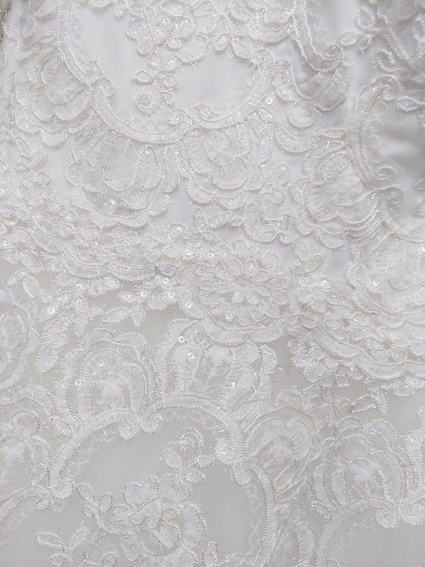 Nina Canacci 1508 is a long Lace Embellished Ivory wedding Dress. Featuring a scallop edge lace fitted bodice with adjustable spaghetti straps. Cascading floral embroidered lace flowing into the full a line ballgown skirt. Great Plus Size Bridal & Destination wedding dress. Sequin Embellished A Line Ballgown. Available Sizes: 8 Available Colors: Diamond White