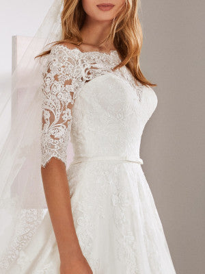 White One OSSA by Pronovias is Probably the wedding dress most little girls have dreamed of; this classic lace tulle gown has the sweetest of necklines with a lace yoke, pretty, lacey school-girl sleeves and a full-blown skirt with a scalloped edge. A Line Lace Ballgown with off the shoulder eyelash three quarter length sheer sleeves. Embroidered Lace Stunning Plus Size Bridal Gown!  Available Size: 28  Available Color: Off White
