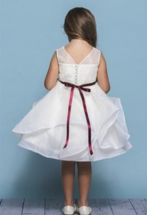 Rosebud Fashions Style 5138 is a knee length dress with a pleated illusion organza bodice. It features an organza asymmetrical skirt with horse hair trim. The waist is accented by a bling ribbon that ties to a bow in the back. Satin buttons cover the zipper. Short Flower Girl Dress, Formal Girls Party Gown.