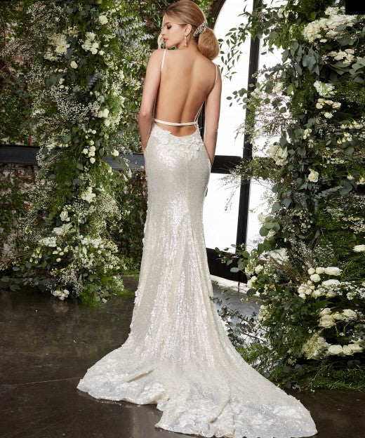 Jovani Bridal JB03592 cream bridal gown features a slim silhouette with a deep plunging neckline, spaghetti straps and a single-strap open back. Three-dimensional floral appliques embellish this sequin wedding dress, finished with a thigh-high slit and a chapel train. Sequin Floral Lace Backless Wedding Dress Slit Train Fitted Available Sizes: 00-24 Available Colors: Cream