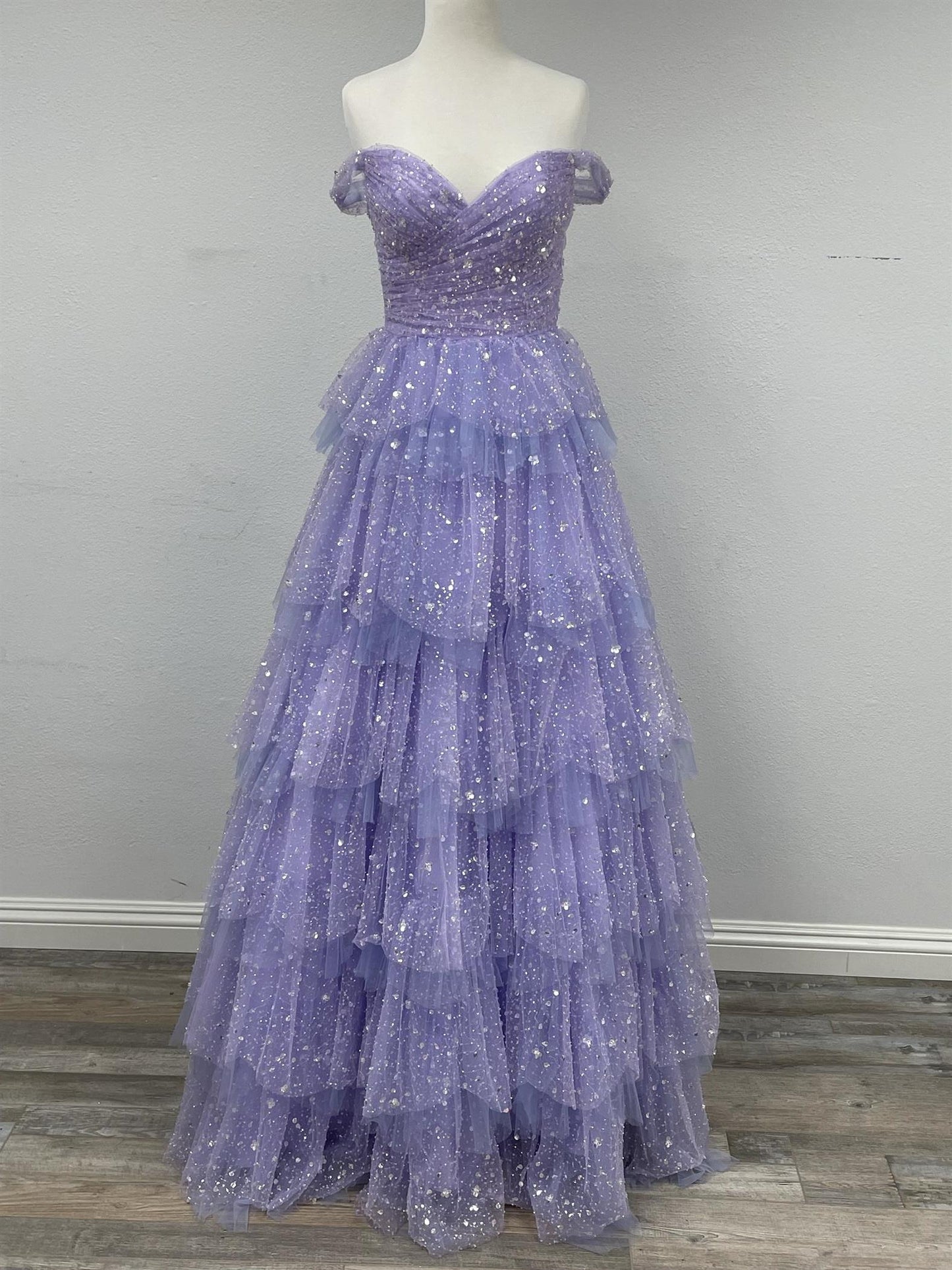 Be the belle of the ball in our Nox Anabel R1315 prom dress. This stunning A-line gown features beautiful sequin detailing and a layered tulle skirt for a truly glamorous look. The off-the-shoulder neckline adds a touch of elegance, making it perfect for your special occasion. Available in size 4 and in a lovely lilac color.  Size: 4  Color: Lilac