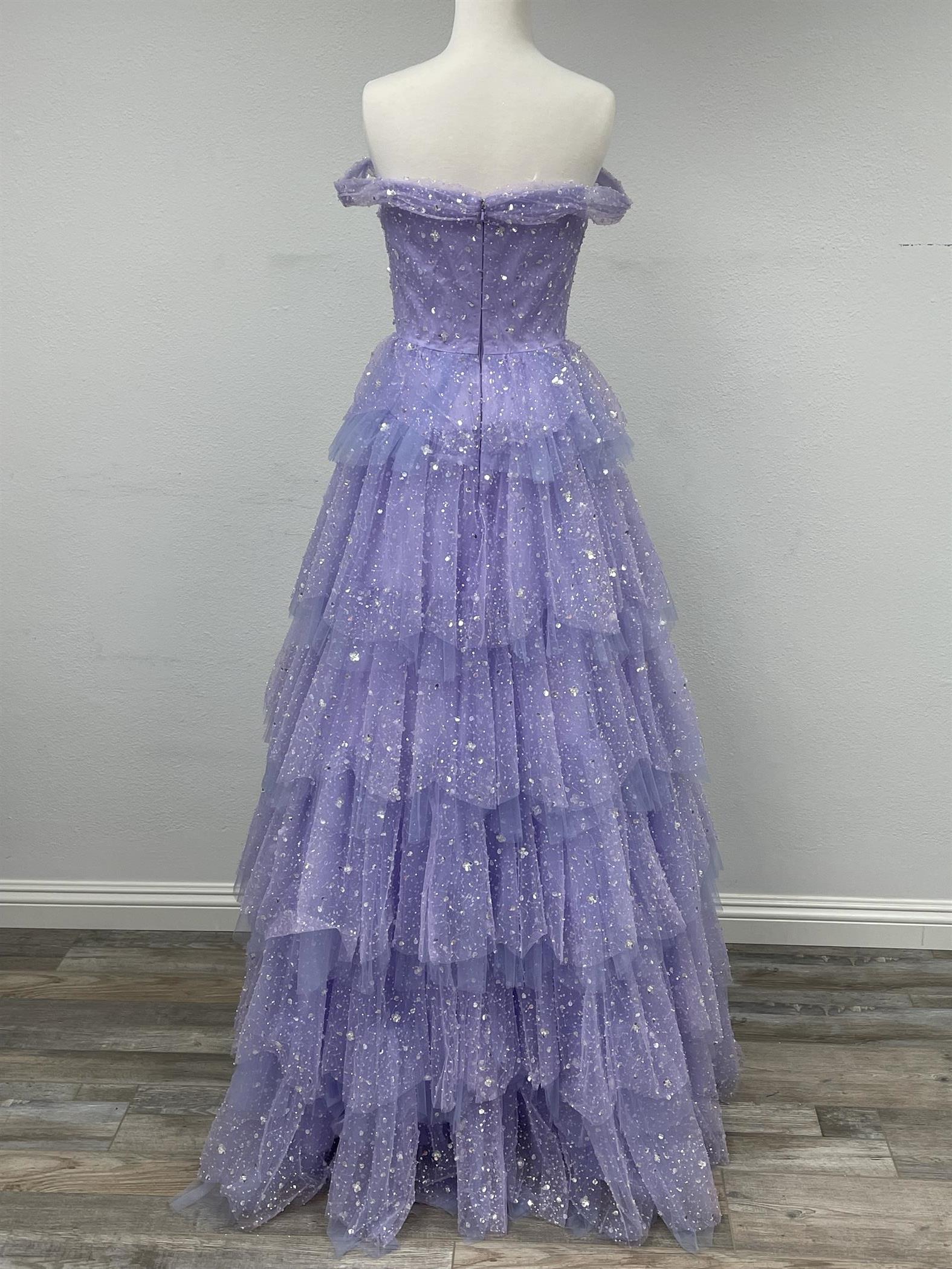 Be the belle of the ball in our Nox Anabel R1315 prom dress. This stunning A-line gown features beautiful sequin detailing and a layered tulle skirt for a truly glamorous look. The off-the-shoulder neckline adds a touch of elegance, making it perfect for your special occasion. Available in size 4 and in a lovely lilac color.  Size: 4  Color: Lilac