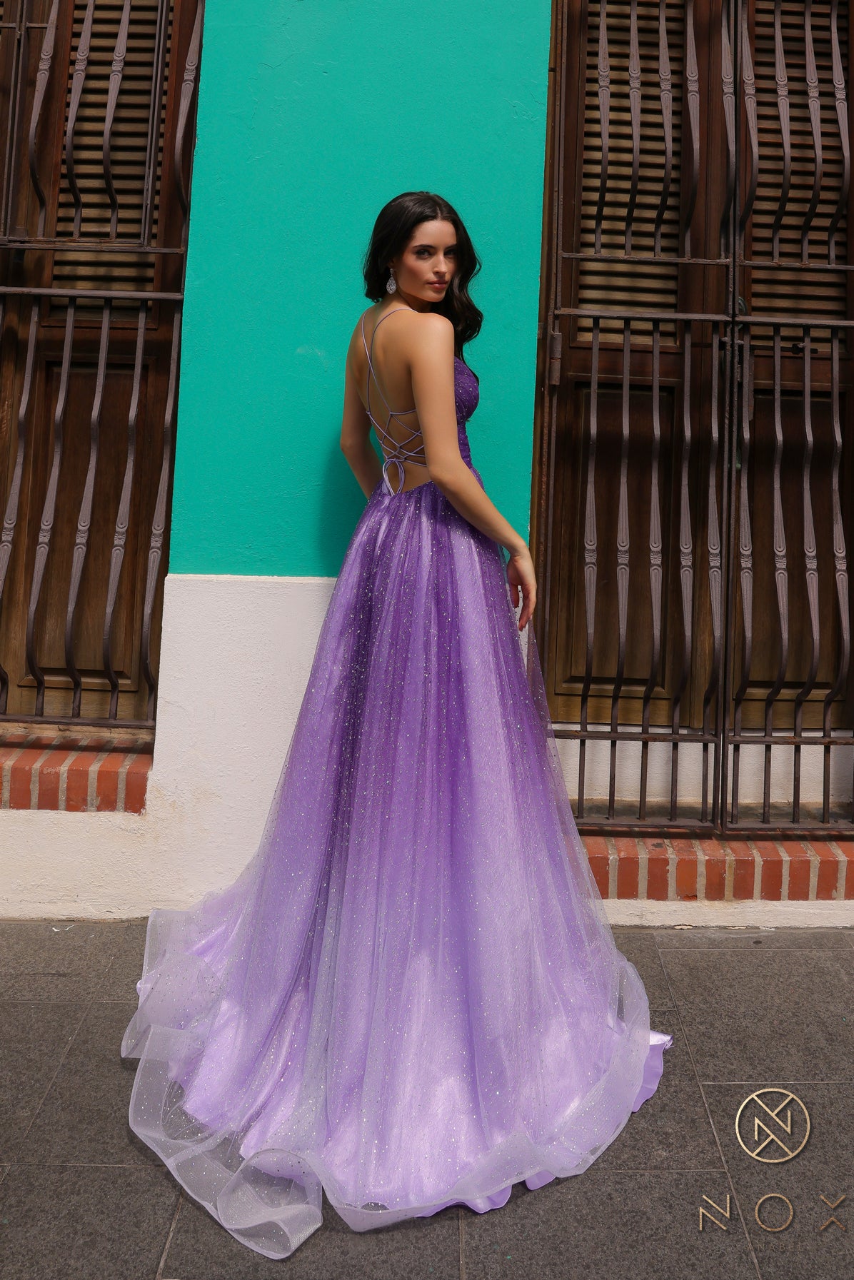 Get ready to make a statement at your next formal event with the Nox Anabel C1251 Long Shimmer Ombre A Line Slit Prom Dress. The backless corset adds a touch of elegance, while the A-line cut and side slit offer a flattering and stylish look. Perfect for prom, weddings, or any special occasion.  Sizes: 00-16  Colors: Purple
