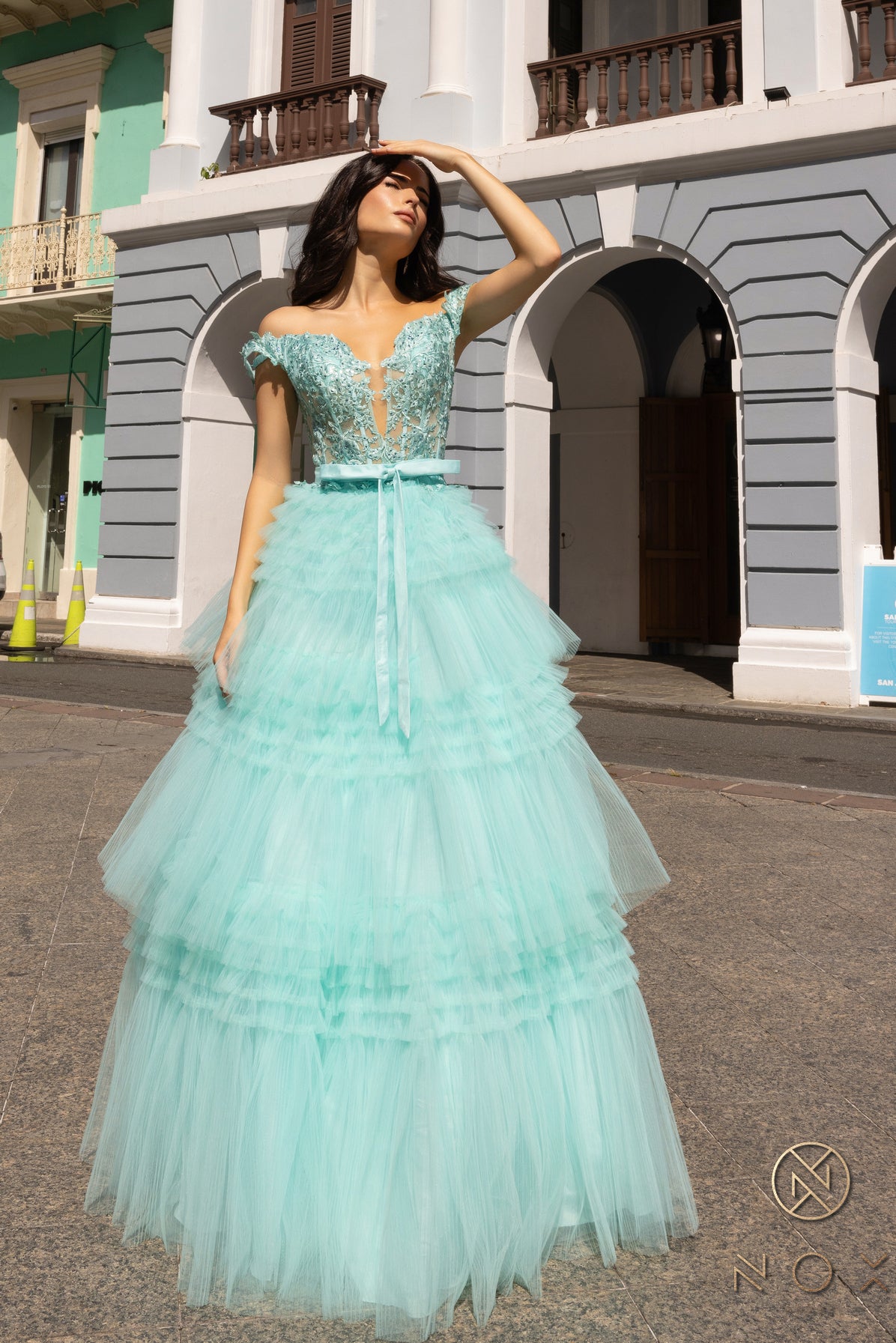 Experience the elegance and sophistication of the Nox Anabel E1293 Prom Dress. With a stunning A-line silhouette, pleated tulle layers, and sheer lace embellished Corset , this dress will make heads turn. Complete with an off-shoulder design and a delicate bow, this dress is perfect for a prom or any formal event.  Sizes: 0-16  Colors: Blue, Mauve, Mint Green, Periwinkle