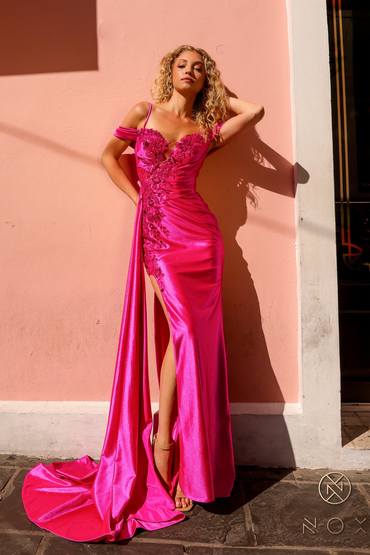 Introducing the Nox Anabel E1451 prom dress, featuring a stunning high slit and off the shoulder lace design. Made with long fitted satin and a sheer illusion bodice, this dress exudes elegance and sophistication. Perfect for prom, pageants, and other formal occasions.  Sizes: 2-16  Colors: Fuchsia, Royal Blue