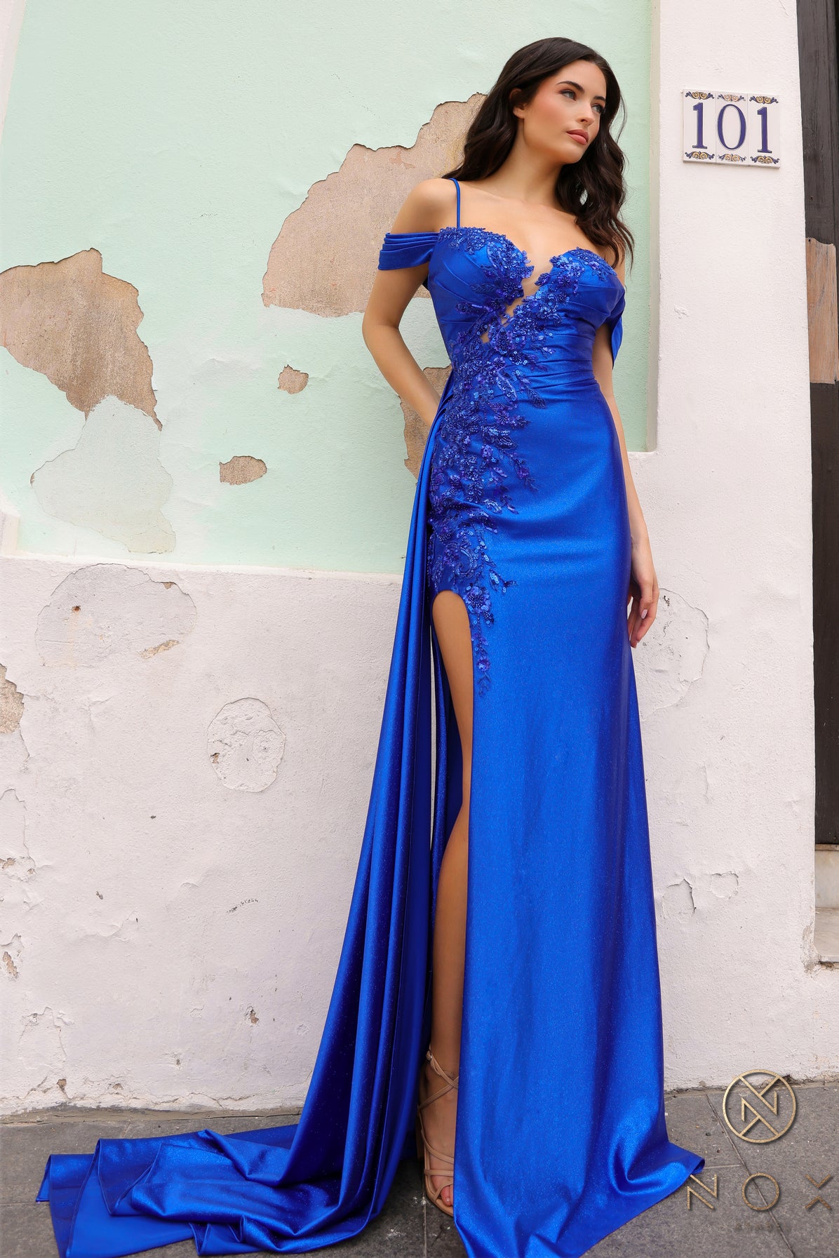 This Nox Anabel E1451 Prom Dress is a stunning choice for any formal occasion. The shimmering lace, off the shoulder design, and elegant overskirt create a beautiful and sophisticated look. With a slit detail and comfortable fit, this dress is perfect for standing out and dancing the night away.
