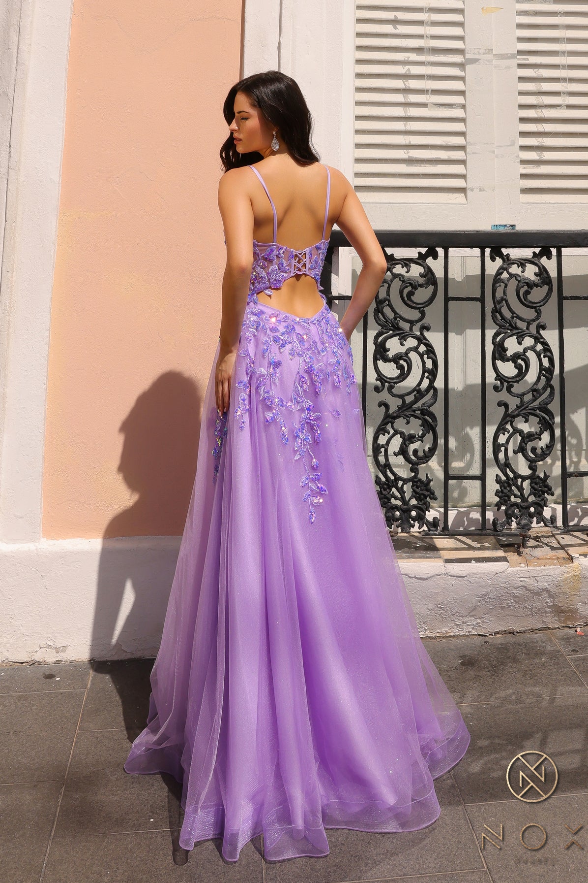 Elevate your style with the Nox Anabel H1350 A Line Maxi Dress. The dress features shimmering tulle and sequin lace, along with a corset bodice and open back cut out design and thigh-high slit. Perfect for formal events, this dress is a must-have for a statement-making entrance.  Sizes: 0-16  Colors: Black, Lavender, Royal Blue
