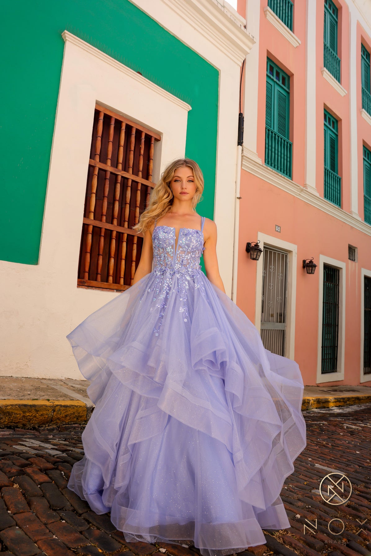 This Nox Anabel H1351 Prom Dress is the perfect combination of elegance and flair. Designed with a shimmering ruffle ballgown and a sheer sequin corset, this dress will make you stand out at any formal event. The v neck adds a touch of sophistication, making you feel like royalty.  Sizes: 0-16  Colors: Hot Pink, Lilac, Orange, Periwinkle, Royal Blue