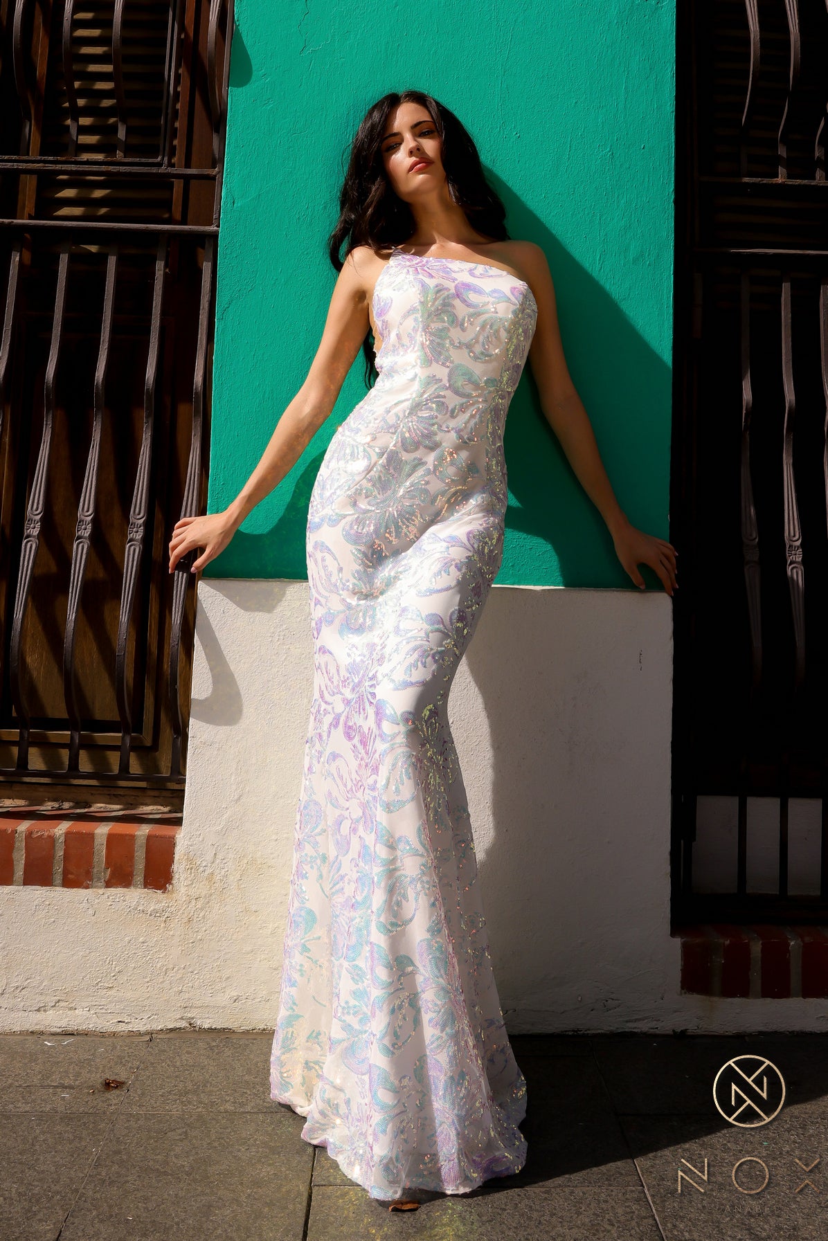 Be the ultimate showstopper in this stunning Nox Anabel R1308 sequin lace one shoulder prom dress. The mermaid silhouette and formal design will give you the confidence to shine on any pageant stage. Guaranteed to make a lasting impression, this gown is a must-have for any special occasion.  Size: 0-16  Colors: Fuchsia, Aqua Blue, White Multi