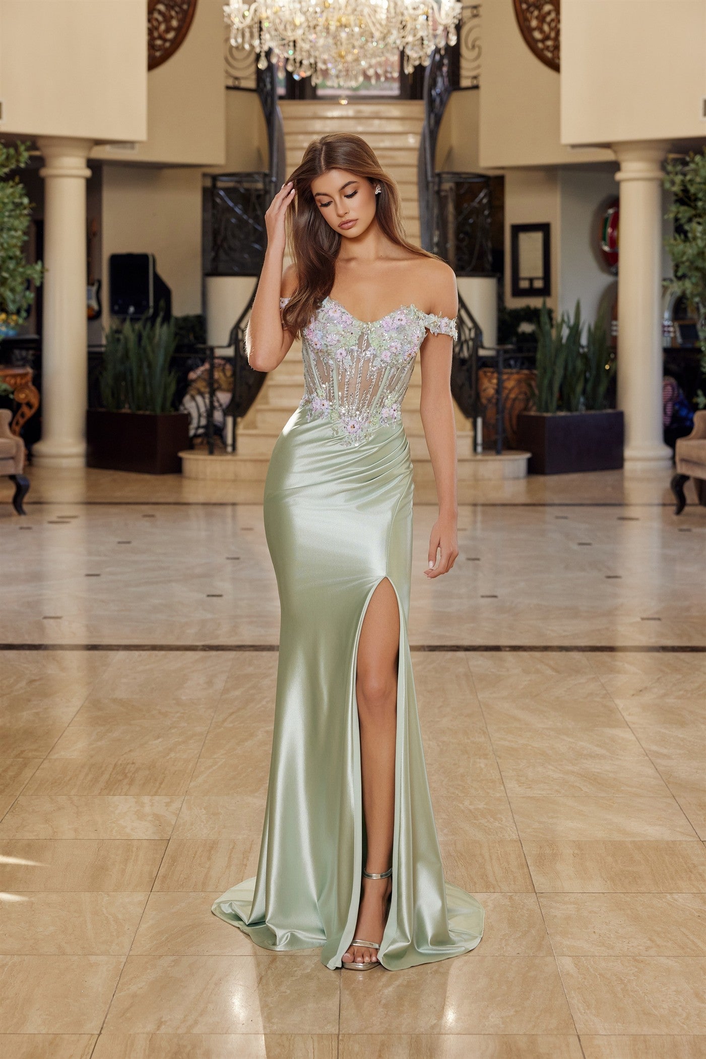 Nox Anabel's R1814 prom dress commands attention with its sophisticated off-the-shoulder silhouette and sheer crystal-embellished corset bodice. The backless satin design flows into an elegant slit train, creating dramatic movement with every step. Perfect for those seeking a statement-making gown that balances glamour with modern edge. This dress celebrates confidence and refined elegance for your most memorable evening.

Sizes: 16

Colors: Powder Blue, Sage Green&nbsp;