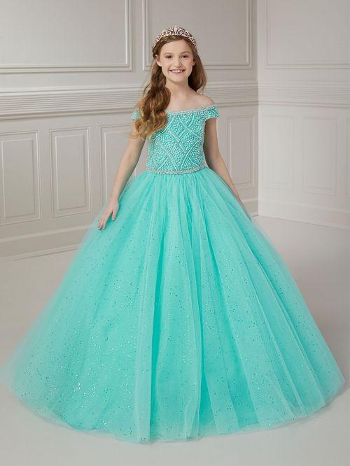 The Tiffany Princess 13722 pageant dress is a stunning option for any young contestant. The crystal and pearl bodice adds a touch of elegance, while the off-the-shoulder neckline and A-line ballgown silhouette create a regal look. Made with tulle, this dress is sure to stand out on stage. <span data-mce-fragment="1">Feel like a princess in this off-the-shoulder neckline with pearls and rhinestone beaded bodice, layers of tulle ball gown skirt and lace-up back closure.</span>