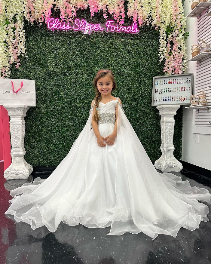Ava Presley 27731 is a beautiful, chiffon A-line pageant ball gown for little girls featuring an off the shoulder cape, crystal-embellished waist, and long maxi skirt. Its exquisite hand-beaded details add a sophisticated and elegant touch, making it the perfect dress for special events.  Sizes: 2  Colors: Off White