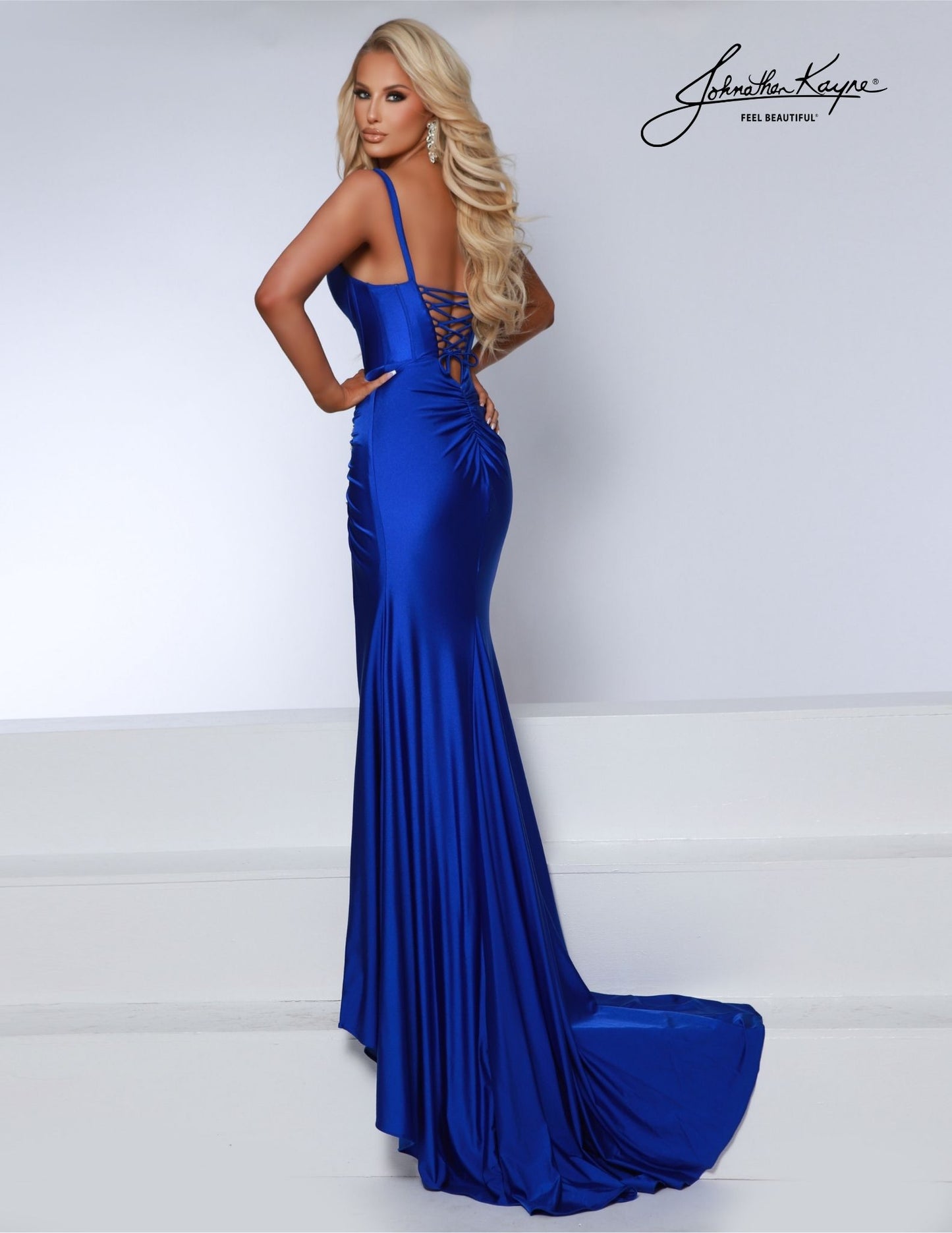 This Johnathan Kayne 2858 prom dress features a corset bodice with crystals, a tail of ruching, a V-neck, and a backless design. Perfect for a formal occasion like a pageant or prom, this silk gown exudes glamour and sophistication. Discover elegance in every detail with our 4-Way Stretch Lycra Gown. This masterpiece features exposed boning, a captivating corset back, and crystal-encrusted ruching, all culminating in a striking ensemble. The slit adds a dash of allure.