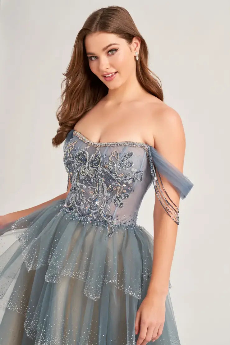 The Ellie Wilde EW35040 prom dress boasts a stunning A-line silhouette adorned with sparkling crystals and sequins. The sheer corset bodice adds a touch of allure, while the off-the-shoulder neckline and beaded fringe details add a trendy touch. Elevate your prom look with this enchanting and figure-flattering dress.  Sizes: 00-16  Colors: Slate, Black/Champagne
