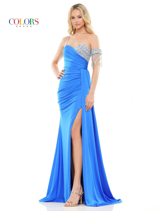 Step onto the red carpet in style with the Colors Dress 3275 Fitted Ruched Slit Overskirt Prom Dress. The one side off the shoulder design is embellished with eye-catching crystal details, while the fitted silhouette is accentuated with a ruched overskirt and fringe detailing. Be the standout at any pageant or prom with this beautiful and glamorous dress.  Sizes: 0-22  Colors: Black, Royal, Deep Green, Hot Pink