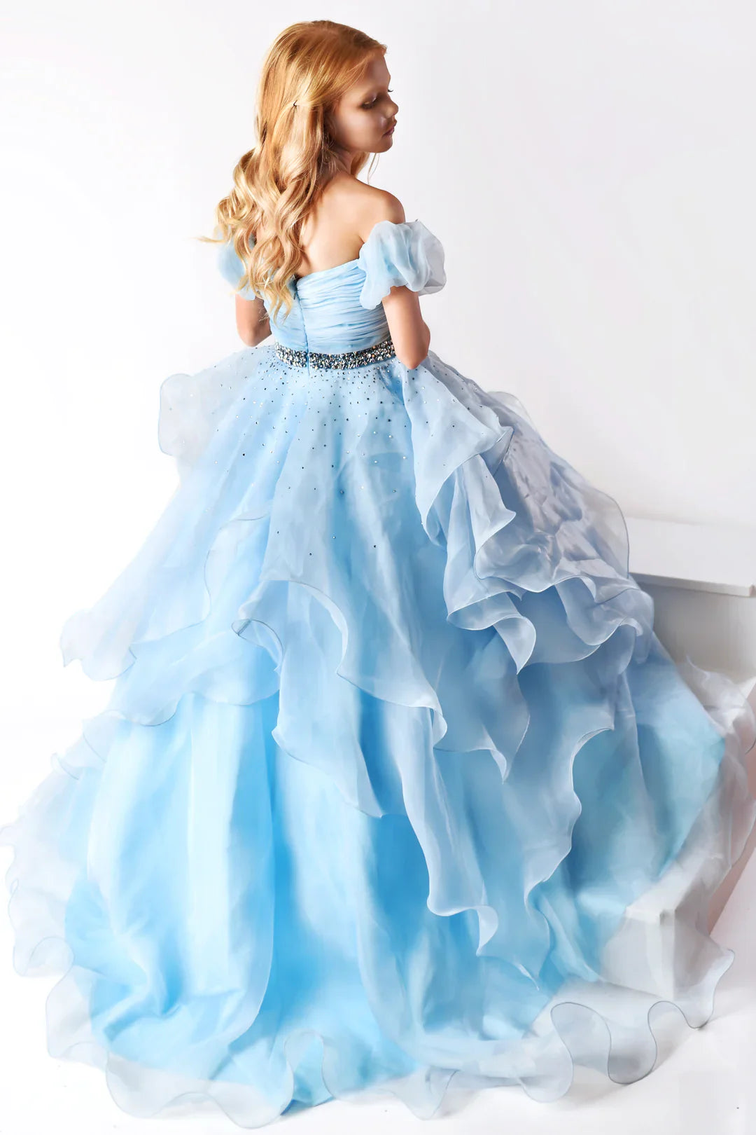 The Ava Presley 38025 Long Ruffle layer A Line Ballgown is designed for girls' pageant wear, offering classic style and sophistication. Its off-the-shoulder design features a puff sleeve, ruffle layer and detailed craftsmanship for an elegant look. Made of soft and durable fabric, it offers superior comfort and long-lasting wear.  Sizes: 2-16  Colors: Light Blue, Coral, White