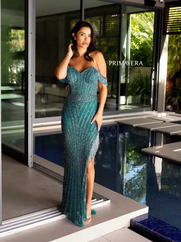 Step into the spotlight with the Primavera Couture 4127 Long Prom Dress. This stunning gown features a trendy off-shoulder neckline, a figure-flattering corset bodice, and intricate sequin and bead detailing. The fringe accents and high slit add a touch of glamour, making it the perfect choice for your next formal event or pageant.