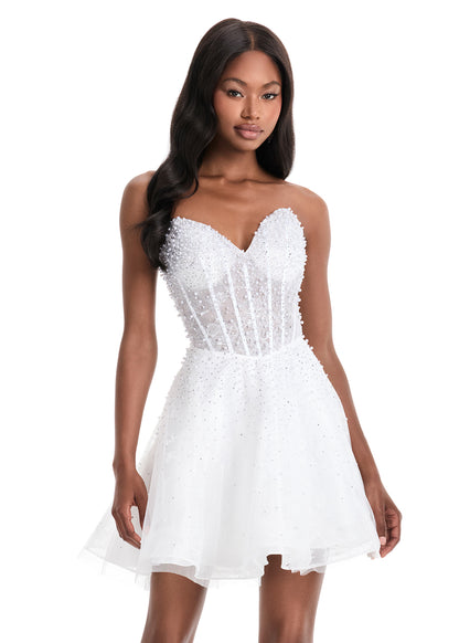 The Ashley Lauren 4924 Short Lace Cocktail Dress combines delicate lace with a sheer corset bodice, adorned with intricate beadwork for subtle elegance. Its fit-and-flare silhouette flatters the figure while providing comfortable movement, making it an excellent choice for formal events or homecoming. This dress balances classic design with modern detailing to create a sophisticated and stylish look. Feel elegant in the ASHLEYlauren Style 4924, a lace dress featuring intricate press-on beading throughout th