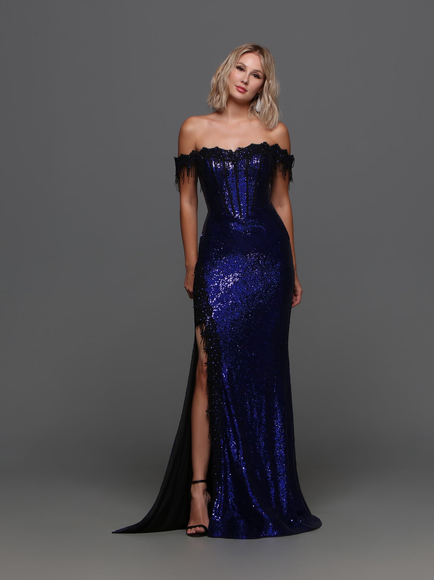 Radiate elegance and sophistication with the Candice Wang 72351 Long Sequin Gown. Featuring an off-the-shoulder lace design and a corset for a figure-flattering fit, this gown also boasts a high sheer slit for a touch of allure. The delicate fringe adds a touch of playful movement to this formal dress.  Sizes: 0-20  Colors: Black, Cobalt/Black   