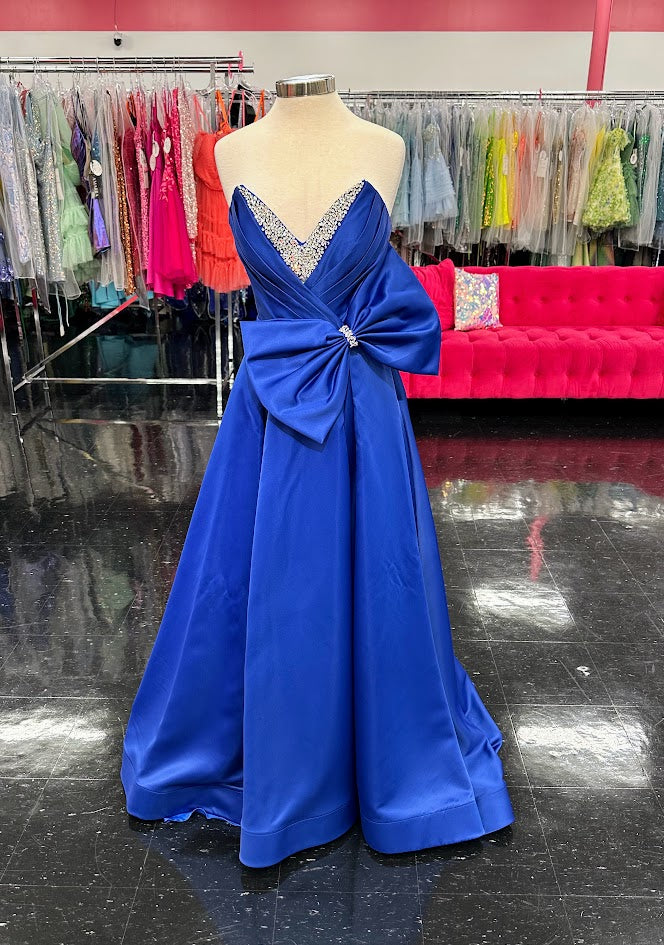 Discover elegance and glamour with the Candice Wang 72499 Royal Satin Maxi Slit A Line Bow Prom Dress. This stunning formal dress features a crystal-embellished V-neck and a gorgeous bow detail. With its A-line silhouette and thigh-high slit, it's perfect for any pageant or prom.&nbsp;

Sizes: 8

Colors: Royal