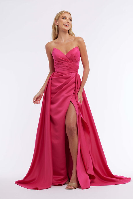 The Vienna Prom 7898 Long Prom Dress is a stunning choice for any formal occasion. With a strapless fitted bodice, ruching detail, and an elegant overskirt, this dress will flatter any figure. The high slit adds a touch of glamour while still maintaining a sophisticated look. Walk into your prom or pageant with confidence in this beautiful gown.