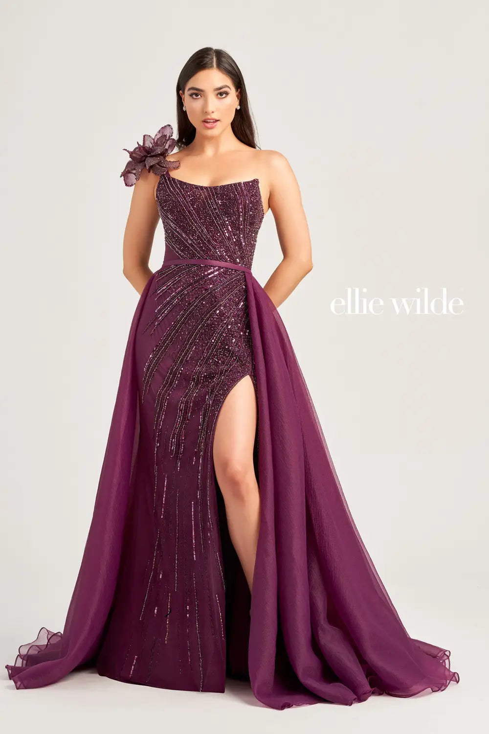 Get ready to turn heads in this stunning Ellie Wilde EW35087 beaded pageant dress. With its shimmering one shoulder bow and elegant scoop neck, this dress exudes sophistication and glamour. The sheer skirt with an organza overskirt and corset lace up back add the perfect touch of drama. Elevate your prom or pageant look with this show-stopping gown.  Sizes: 00-20  Colors: Tan, Aubergine