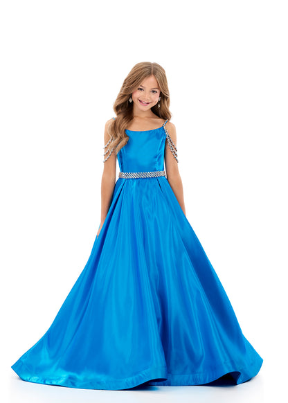 Ashley Lauren 8333, a stunning satin A-line gown designed for young competitors. This sophisticated dress features shimmering fabric that catches the light beautifully, complemented by elegant crystal-embellished off-the-shoulder straps that frame the neckline with glamour. The coordinating belt cinches the waist for a polished silhouette, while practical hidden pockets add functionality without compromising style. The flowing A-line skirt creates graceful movement on stage, ensuring your daughter commands 