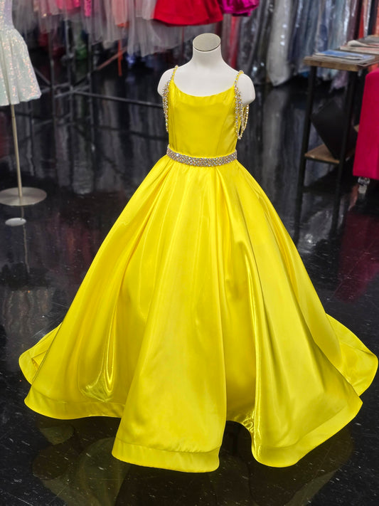 Ashley Lauren 8333, a stunning satin A-line gown designed for young competitors. This sophisticated dress features shimmering fabric that catches the light beautifully, complemented by elegant crystal-embellished off-the-shoulder straps that frame the neckline with glamour. The coordinating belt cinches the waist for a polished silhouette, while practical hidden pockets add functionality without compromising style. The flowing A-line skirt creates graceful movement on stage, ensuring your daughter commands 