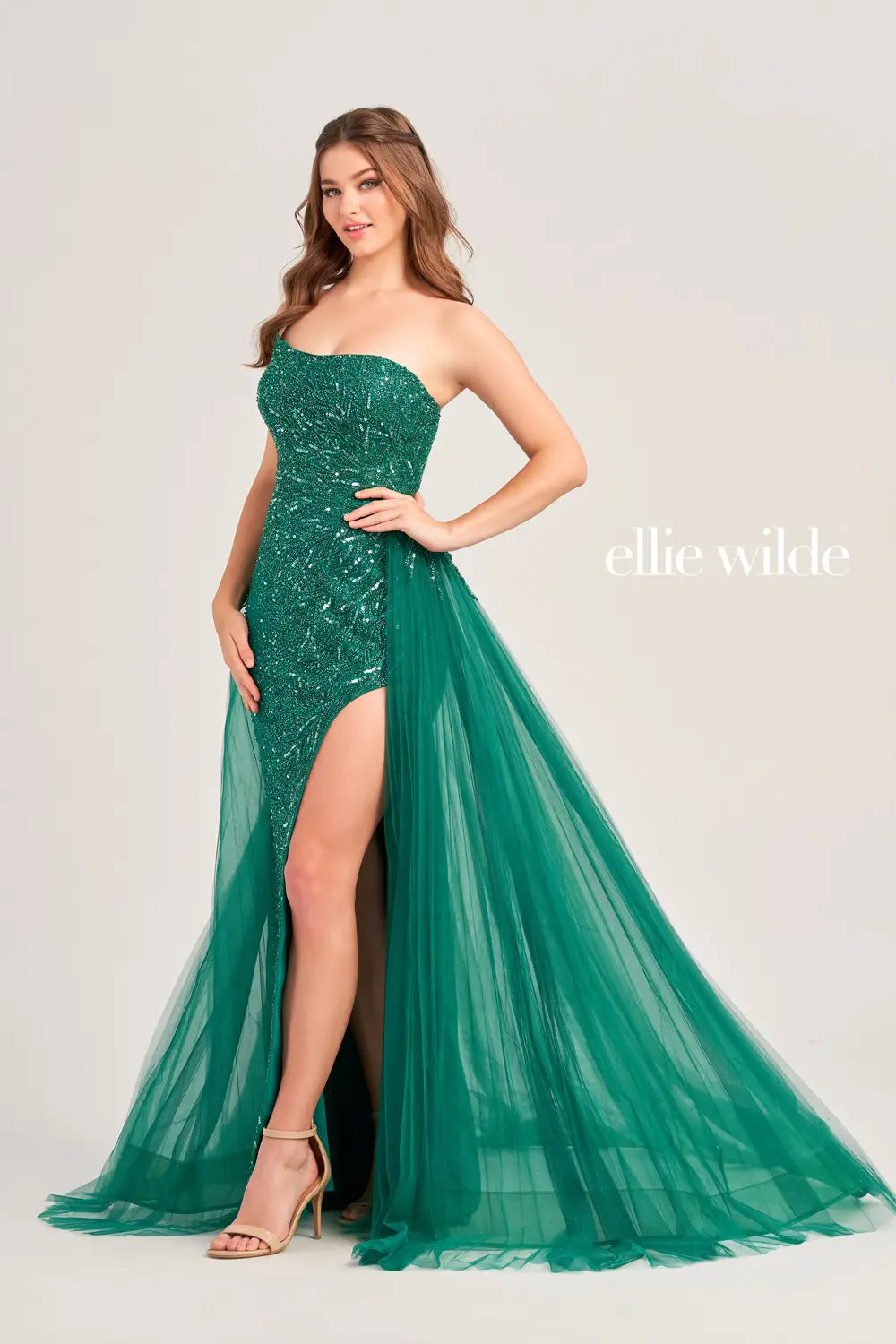 Elevate your formal look with the Ellie Wilde EW35085 Strapless Crystal Pageant Dress. Crafted with a high slit and pleated detachable overskirt, this gown exudes elegance and sophistication. The strapless design and crystal embellishments add a touch of glamour, perfect for any special occasion.  Sizes: 00-16  Colors: Coffee, Emerald