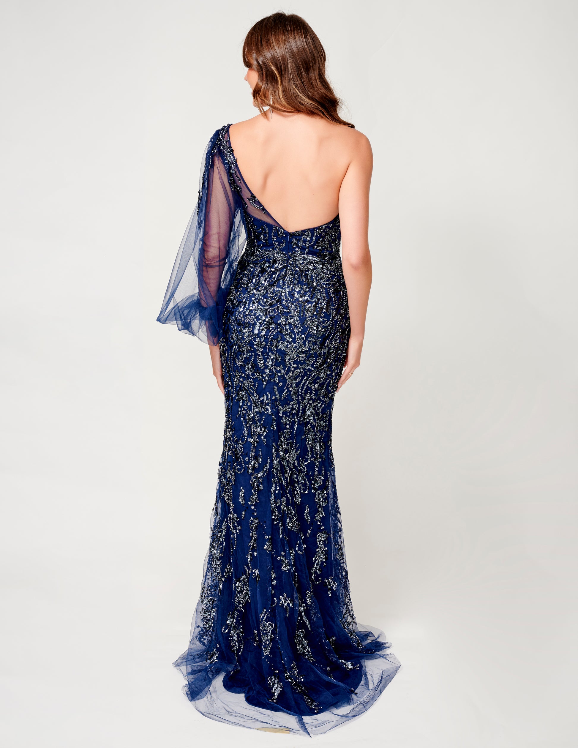Elevate your evening style with this stunning Nina Canacci 9159 Navy Beaded Evening Gown. Featuring a flattering one shoulder neckline and elegant long sleeve, this formal gown is adorned with intricate beadwork for a touch of glamour. The side slit adds a touch of allure to this timeless and sophisticated piece. Perfect for any special occasion, this gown is sure to make a statement. Moth of Gown