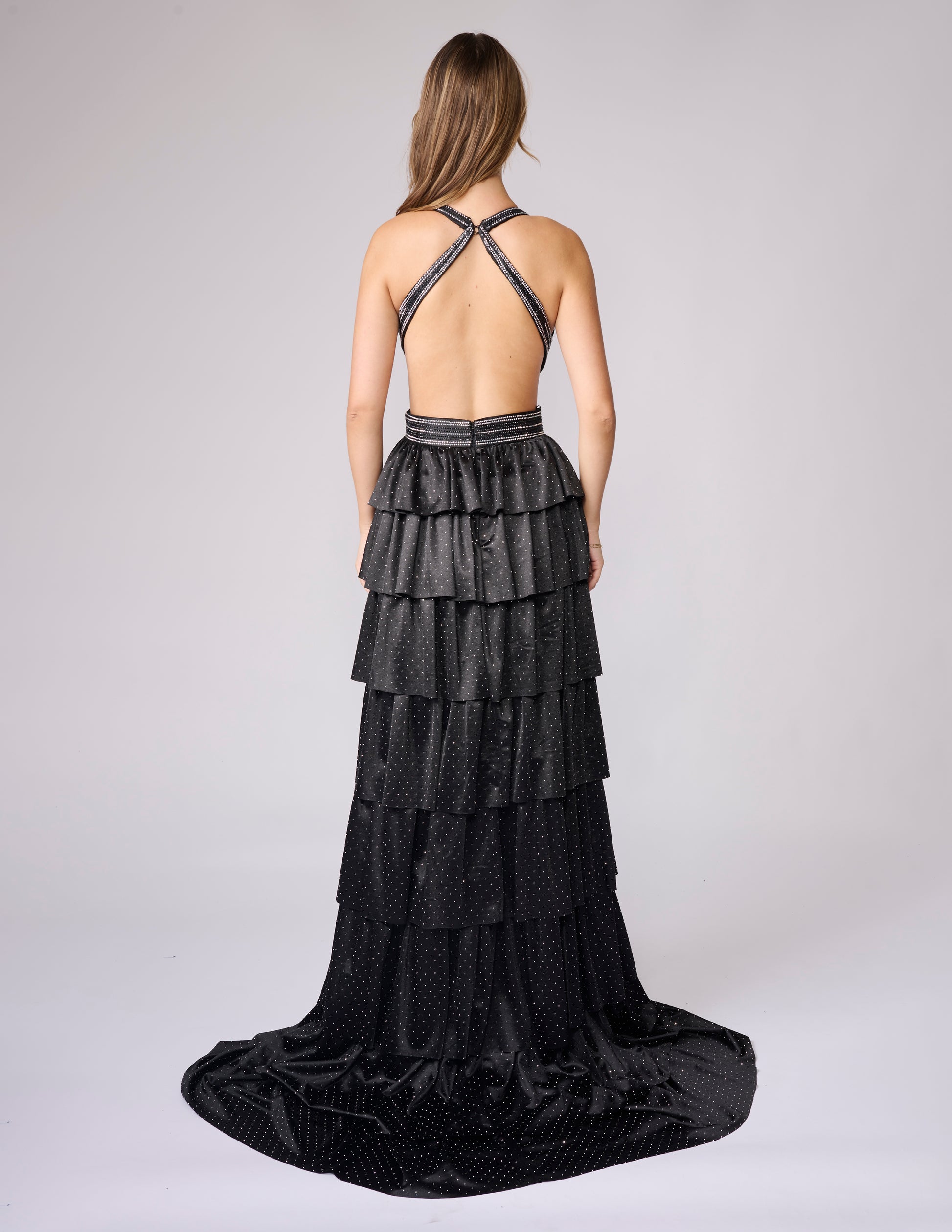 Nina Canacci's 9200 is a show-stopping pageant gown that combines elegance with contemporary flair. The crystal-layered jersey skirt features intricate micro crystal embellishments that catch light beautifully, while strategic side cutouts add modern sophistication. A dramatic maxi slit and flowing train create movement and grandeur, making this dress ideal for prom, pageants, and formal competitions. The jersey construction ensures comfortable wear throughout the evening while maintaining a polished silhou