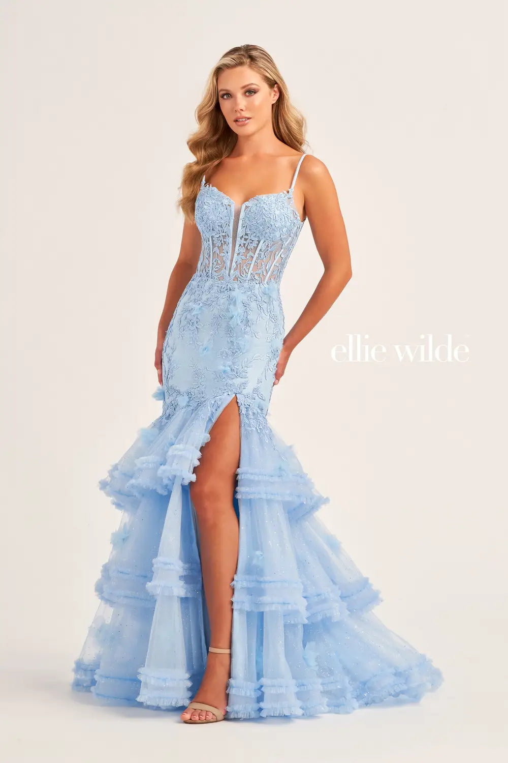Be the star of the night in this Ellie Wilde EW35050 prom dress. The sheer lace corset with 3D dimensional appliques creates a flattering silhouette while the Tiered Tulle pleated ruffle layered trumpet skirt features a slit and shimmer fabric add a touch of glamour. The pleated mermaid skirt and slit offer both elegance and comfort.  Sizes: 00-16  Colors: OCEAN BLUE, LIGHT BLUE, HOT PINK
