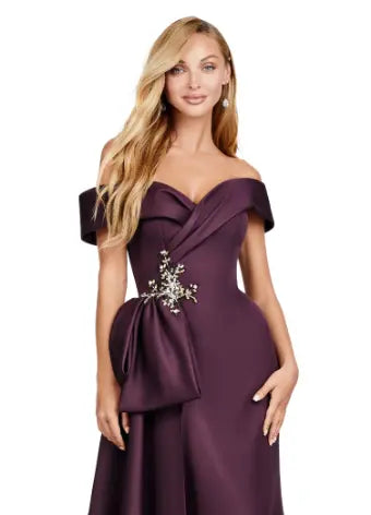 This Ashley Lauren 11425 Long Wine Evening Mother of Dress is the perfect choice for any formal occasion. The off-shoulder design adds a touch of elegance, while the fitted satin fabric hugs your figure for a flattering silhouette. The overskirt adds a dramatic flare, making you feel like a pageant queen. Elevate your style with this versatile and stunning dress. An elegant off the shoulder neckline drapes the shoulders in elegant evening gown. The look is complete with beaded details and a side overskirt.