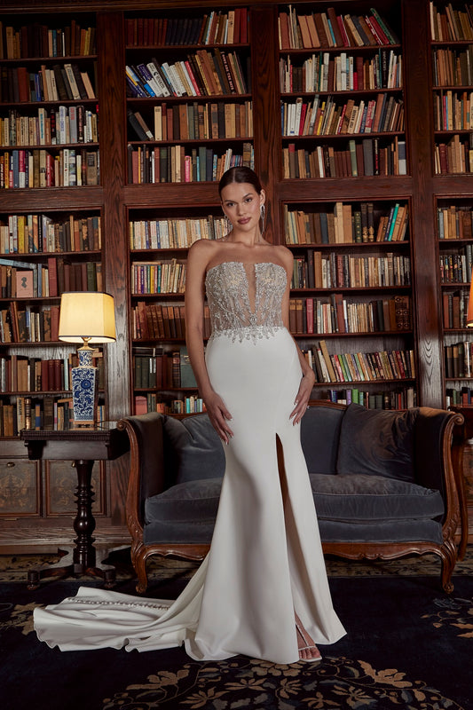 Casablanca Bridal 2538 Belle Wedding Dress.   Minimalist with a touch of glam, this sheath dress in stretch satin with thigh high slit is classic glam. 2538 Belle features a straight across neckline, accompanied by a plunging neckline for a daring vibe.  For an extraordinary touch, our signature hand crafted beading adorns the front and back bodice in silver beading with beaded buttons flowing down the backside of the skirt. Pair Belle with her matching cathedral veil.    Available In: Ivory/Nude/Silver