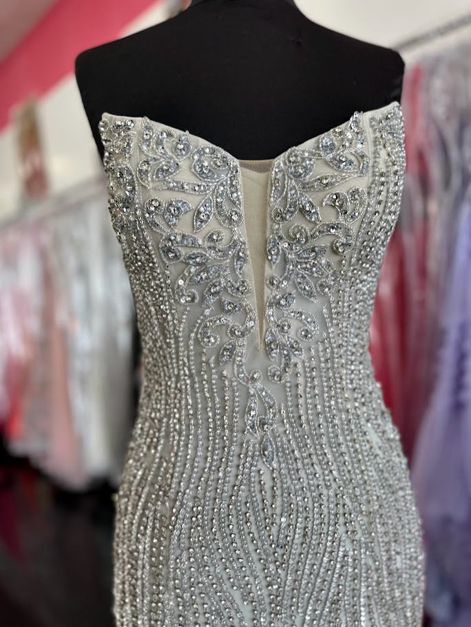 This expertly crafted Chic and Holland HF110284 gown in size 0 features a stunning silver crystal embellishment that elevates the fitted silhouette. Designed with a high slit, it offers graceful movement and a striking profile. The illusion scoop neck gracefully transitions into a V-neckline, combining elegance with modern couture appeal. Perfect for pageants or formal events, this gown balances sophistication and glamour to ensure unforgettable presence.

Size 0&nbsp;

Color: Silver