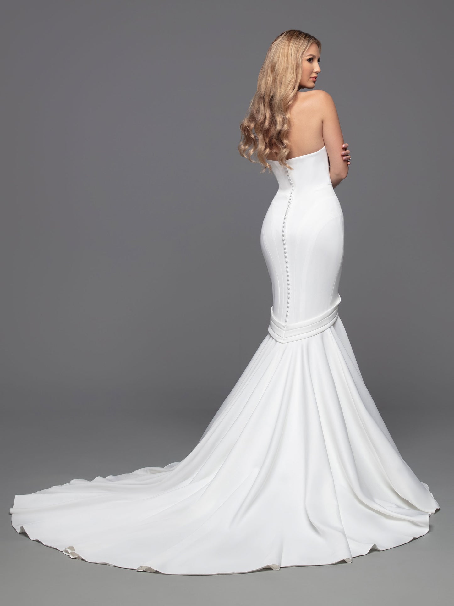 Experience an unforgettable wedding day with this luxurious bridal gown from Davinci. Crafted from alluring ivory fabric, this fit-and-flare mermaid gown is perfected with a strapless, straight-across neckline, a modest silhouette, and an open back with interesting button details and a zipper fastening. The chapel train adds a truly elegant touch.