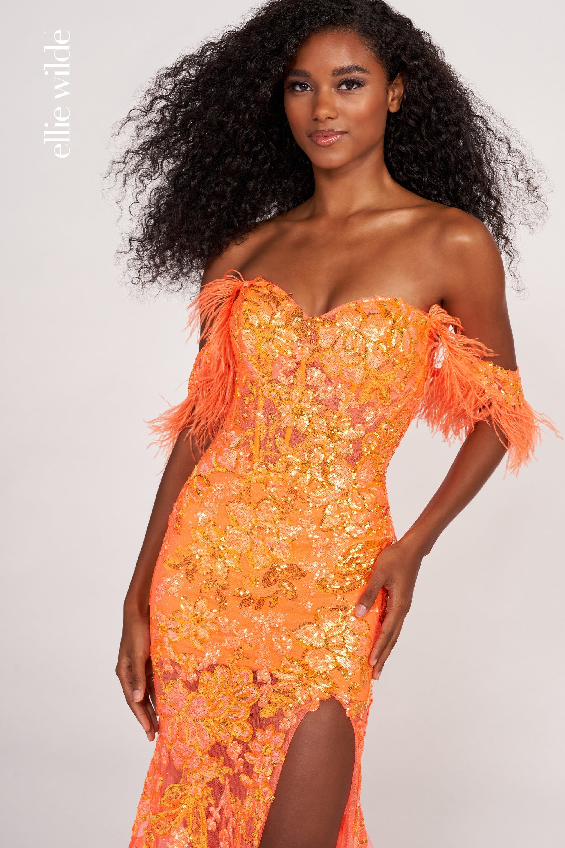 The Ellie Wilde EW34034 is a glamorous formal gown featuring an off-the-shoulder neckline, corset bodice, and a full-length sheer sequin skirt with a side slit. Festooned with a beautiful feather trim, this dress is sure to make a statement.  Sizes: 00-16  Colors: ORANGE, ROYAL BLUE, LILAC, HOT PINK, SAPPHIRE, SKY BLUE, EMERALD, PURPLE RAIN