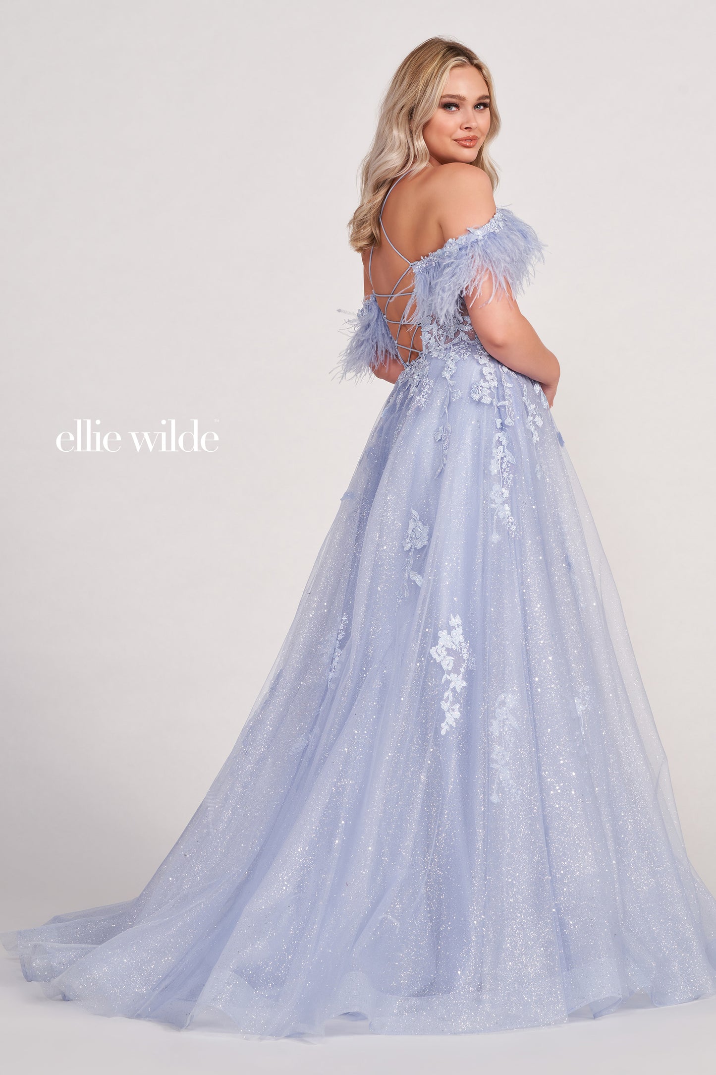 The Ellie Wilde EW34066 is a stunning A-line gown with a sheer sequin corset and feather off-the-shoulder detail. Boasting a dazzling shimmer finish and dramatic slit, this exquisite dress will make you the belle of the ball.  Sizes: 00-16  Colors: ORANGE, RED, PERIWINKLE, IRIS