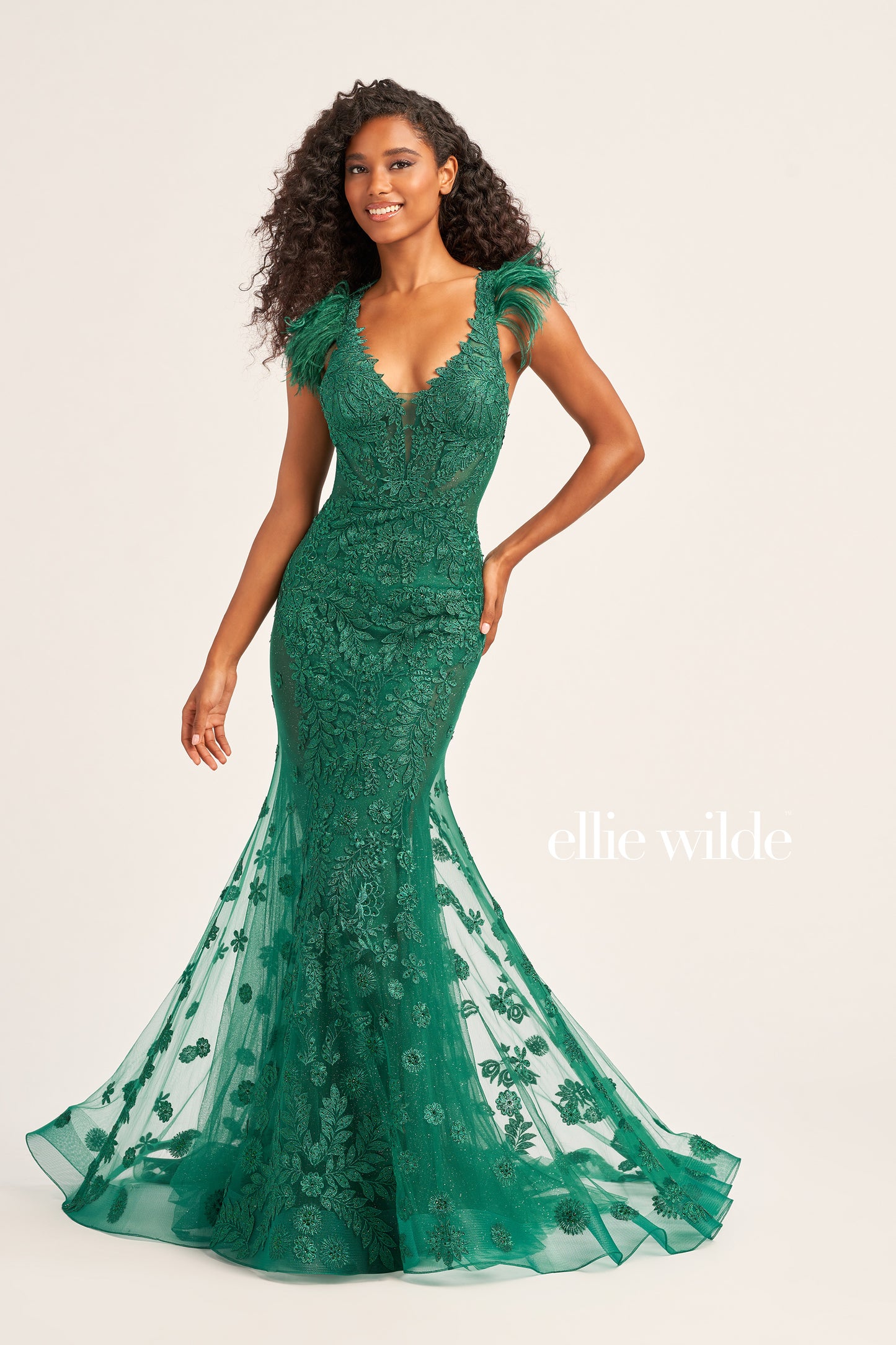 Look dazzling in this Ellie Wilde EW35009 evening gown, crafted with glitter tulle, lace appliques, and stone accents for an eye-catching look. A plunging V-neck, long trumpet silhouette, and detachable feather cap sleeves add to the glamour. The natural waistline and side mesh inset complete the look.  COLOR: BLACK, EMERALD, SAGE, STRAWBERRY, BLUEBELL SIZE: 00 - 20