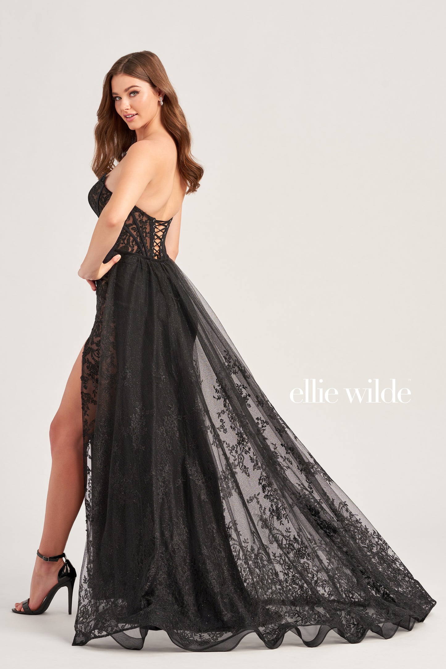 Be prepared to stun in this Ellie Wilde EW35032 long prom dress. Featuring a scoop neckline, glitter lace and stone accents, with a lace up grommet back and high slit for added flair. The corset bodice and detachable train ensure you make a statement. Crafted with stretch jersey for a comfortable fit-and-flare silhouette.  COLOR: BLACK, EMERALD, ROYAL BLUE, RUBY, IRIS, WHITE