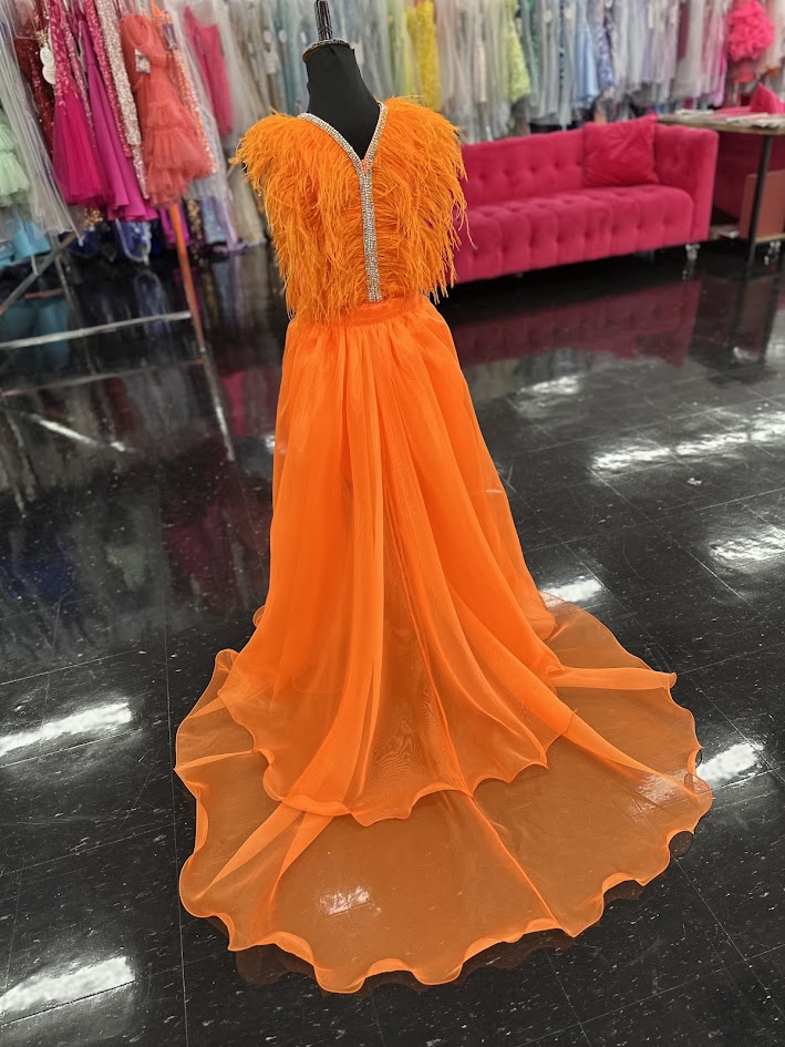Marc Defang's 8308 showcases expert pageant design in size 12, featuring a striking orange romper paired with an elaborate feathered overskirt. This sophisticated ensemble balances practicality with theatrical impact—the fitted romper provides stability and comfort during competition, while the cascading feather overlay delivers the glamorous presence judges expect. The vibrant orange hue commands attention under stage lighting, and the feather detailing adds dimension and movement with every step. An excel