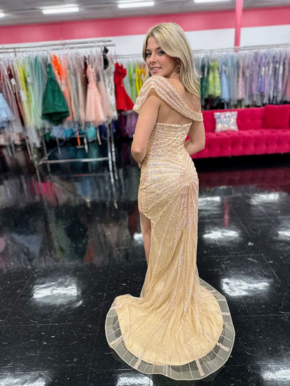 The Nox Anabel H1669 in size 4 is a meticulously crafted champagne-colored gown designed for formal occasions. Its long, fitted silhouette is enhanced by detailed beadwork and sequins, offering a refined shimmer that catches the light elegantly. The gown features a sophisticated slit, providing both movement and subtle allure. A standout element is the detachable asymmetrical off-the-shoulder cape sleeve, which adds versatility and a modern edge to the classic design. This dress combines expert tailoring wi
