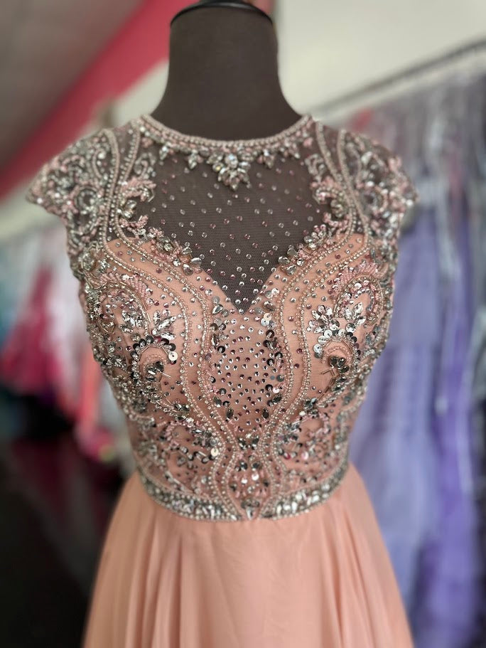 Elevate your formal occasion with the Johnathan Kayne 2750, a size 4 charcoal A-line gown designed for timeless elegance. Featuring a beaded high neckline and delicate cap sleeves, this dress combines refined detailing with a flowing chiffon train for graceful movement. Perfect for the mother of the bride or any distinguished event, it offers a sophisticated silhouette that enhances your presence with understated glamour.

Size: 4

Color: Blush