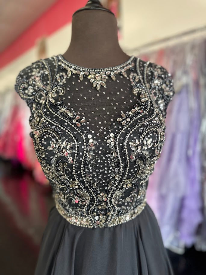 Elevate your formal occasion with the Johnathan Kayne 2750, a size 4 charcoal A-line gown designed for timeless elegance. Featuring a beaded high neckline and delicate cap sleeves, this dress combines refined detailing with a flowing chiffon train for graceful movement. Perfect for the mother of the bride or any distinguished event, it offers a sophisticated silhouette that enhances your presence with understated glamour.

Size: 4

Color: Charcoal