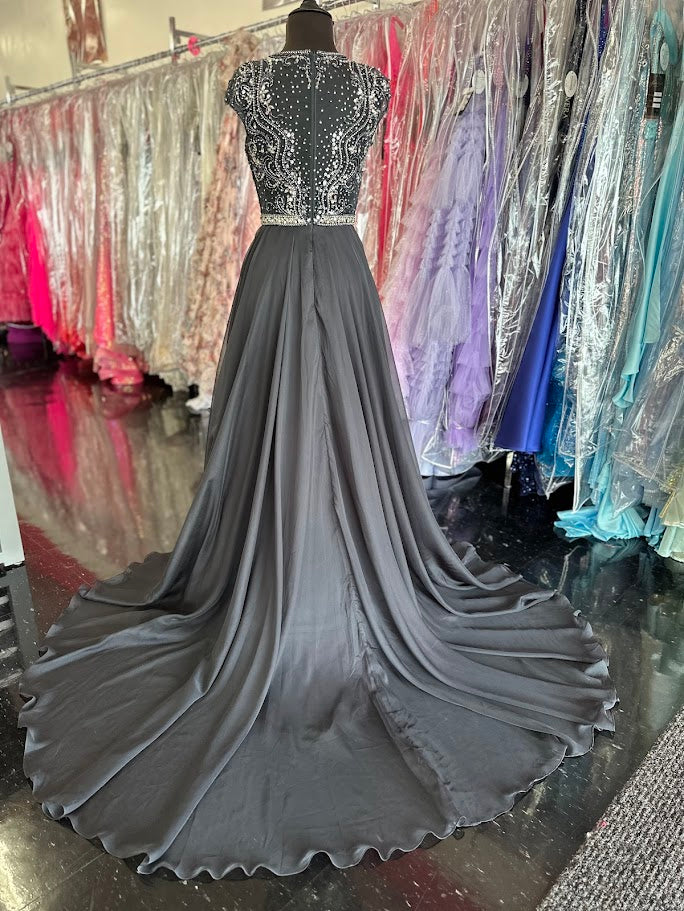 Elevate your formal occasion with the Johnathan Kayne 2750, a size 4 charcoal A-line gown designed for timeless elegance. Featuring a beaded high neckline and delicate cap sleeves, this dress combines refined detailing with a flowing chiffon train for graceful movement. Perfect for the mother of the bride or any distinguished event, it offers a sophisticated silhouette that enhances your presence with understated glamour.

Size: 4

Color: Charcoal