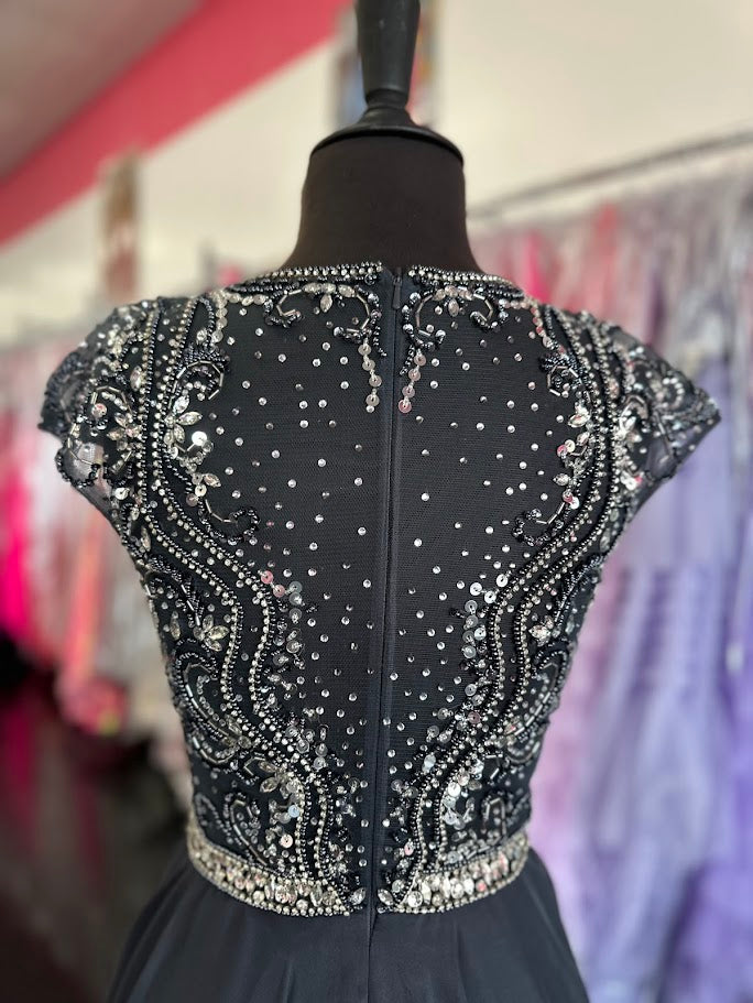 Elevate your formal occasion with the Johnathan Kayne 2750, a size 4 charcoal A-line gown designed for timeless elegance. Featuring a beaded high neckline and delicate cap sleeves, this dress combines refined detailing with a flowing chiffon train for graceful movement. Perfect for the mother of the bride or any distinguished event, it offers a sophisticated silhouette that enhances your presence with understated glamour.

Size: 4

Color: Charcoal